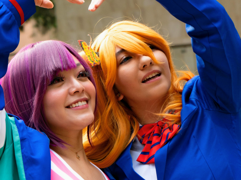 Kaksi cosplay-harrastajaa ovat vierekkäin ja tekevät yhdessä käsillään ison sydämen päidensä yläpuolelle.